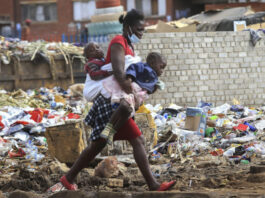 A woman carrying two children walks past a garbage dump amid the third wave of the Covid-19 pandemic in Harare, Zimbabwe on 21 April 2021. (Photo: EPA-EFE / Aaron Ufumeli)