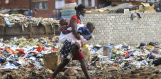 A woman carrying two children walks past a garbage dump amid the third wave of the Covid-19 pandemic in Harare, Zimbabwe on 21 April 2021. (Photo: EPA-EFE / Aaron Ufumeli)