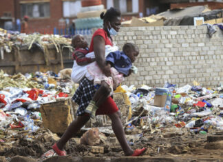 A woman carrying two children walks past a garbage dump amid the third wave of the Covid-19 pandemic in Harare, Zimbabwe on 21 April 2021. (Photo: EPA-EFE / Aaron Ufumeli)