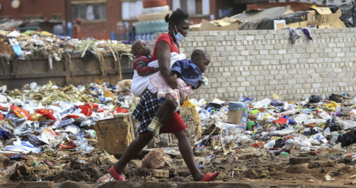A woman carrying two children walks past a garbage dump amid the third wave of the Covid-19 pandemic in Harare, Zimbabwe on 21 April 2021. (Photo: EPA-EFE / Aaron Ufumeli)