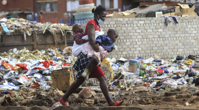 A woman carrying two children walks past a garbage dump amid the third wave of the Covid-19 pandemic in Harare, Zimbabwe on 21 April 2021. (Photo: EPA-EFE / Aaron Ufumeli)